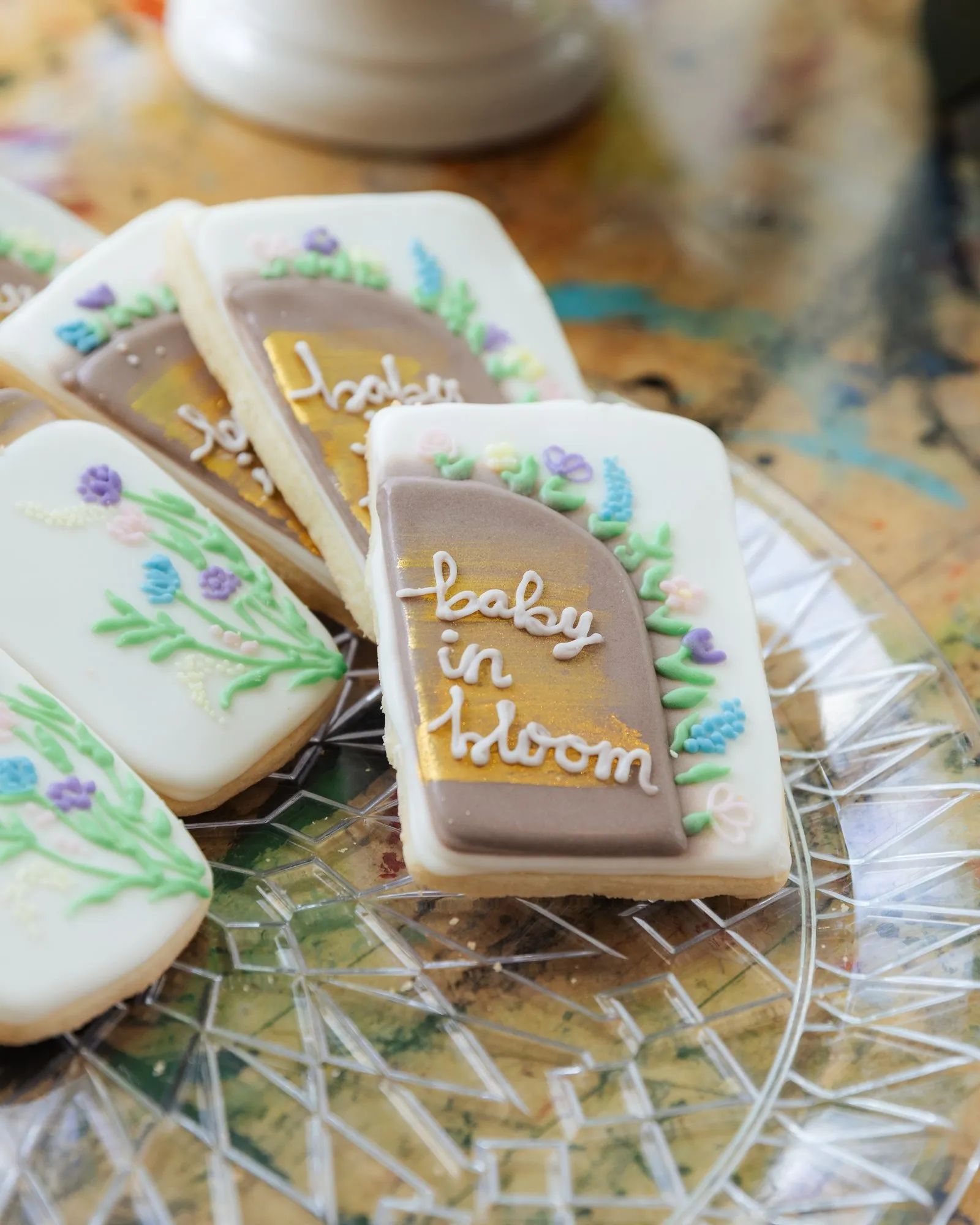 Hand-iced cookies with wildflowers, one lettered "baby in bloom", on a cut-glass plate