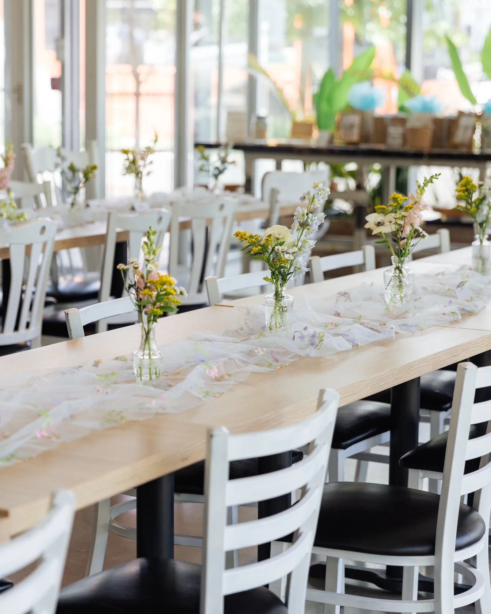 Rows of long tables with white chairs, tulle runners and wildflower bud vases