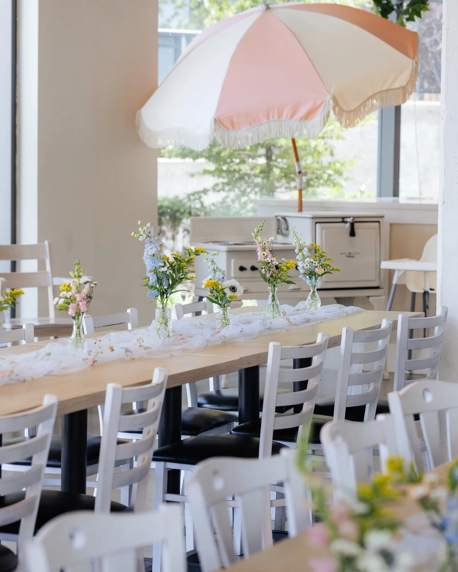 Long tables with wildflower bud vases beside a pink and cream fringed umbrella